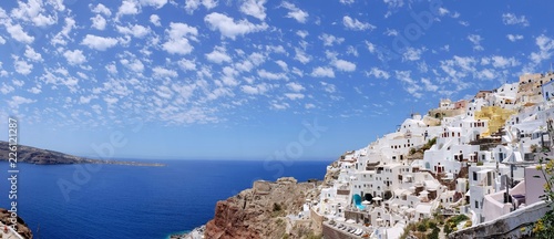 Panoramic aerial view of beautiful white washed buildings against blue sky, clouds and vivid sea in Santorini island, Oia, Greece