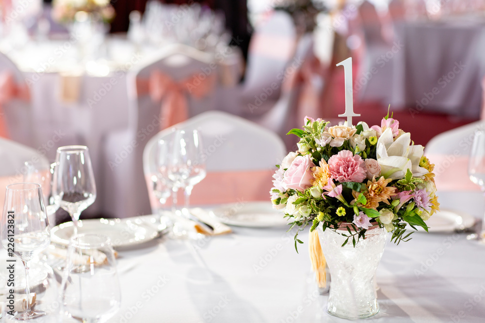 Round table at a luxury wedding reception. Beautiful flowers on the table. Serving dishes, glass glasses, waiters work,
