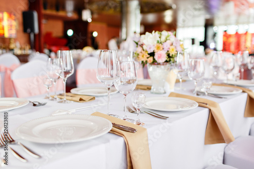 Table at a luxury wedding reception. Beautiful flowers on the table. Serving dishes, glass glasses, waiters work,