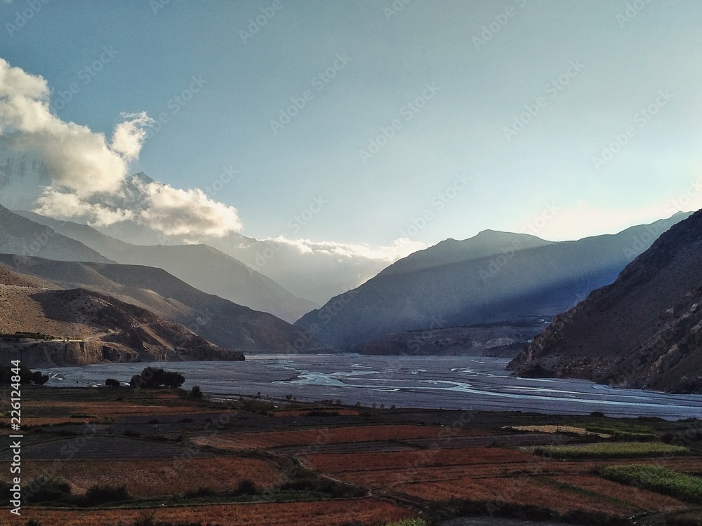 Gorge of the Kali Gandaki river with high cliffs and the valley with farm fields and sunset rays Gorge of the Kali Gandaki river with high cliffs and the valley with farm fields and sunset rays