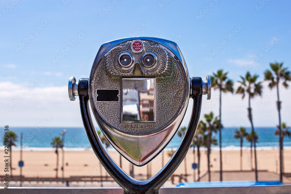 Coin operated binoculars looking out over the ocean and a beach with palm trees.
