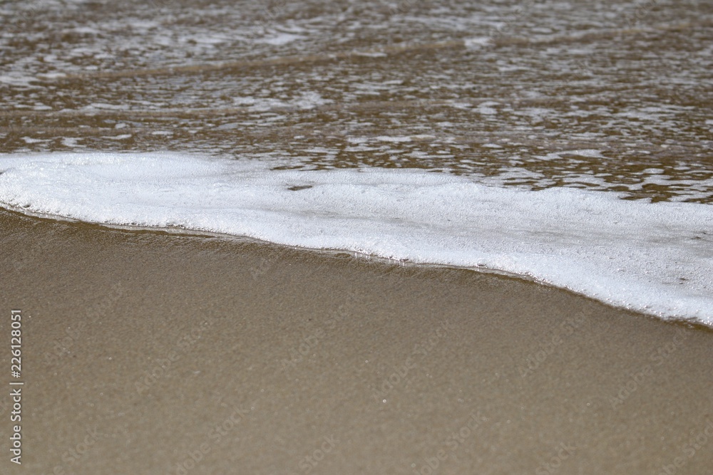 ocean sea foam washing up on a sandy beach 
