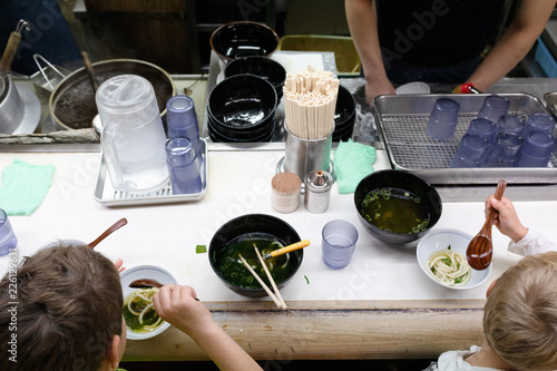 Two blond boys sitting at the counter, eating soup at the local eatery or food stall in Japan