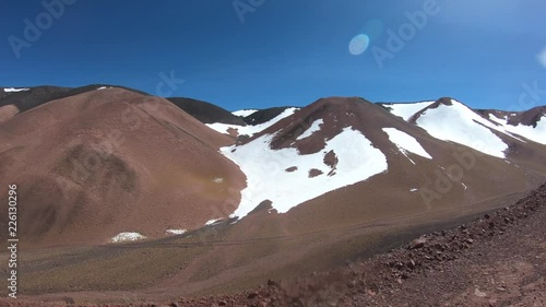 Traveling through gravel road between black, red and yellow mountain landscape. Desertic slopes with snow and grasses at altiplane of The Andes. Excursion to Brava Lagoon, Rioja Province, Argentina photo