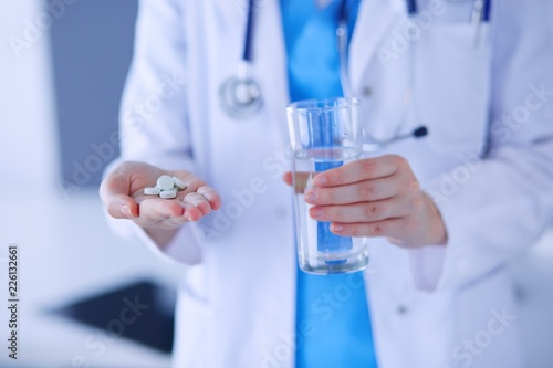Close-up shot of doctor's hands holding pills and glass of water.