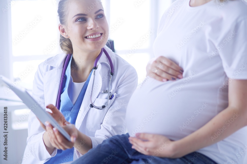Smiling woman doctor shows pictures on the tablet to pregnant young woman at hospital. Smiling woman doctor shows pictures on the tablet to pregnant young woman at hospital.