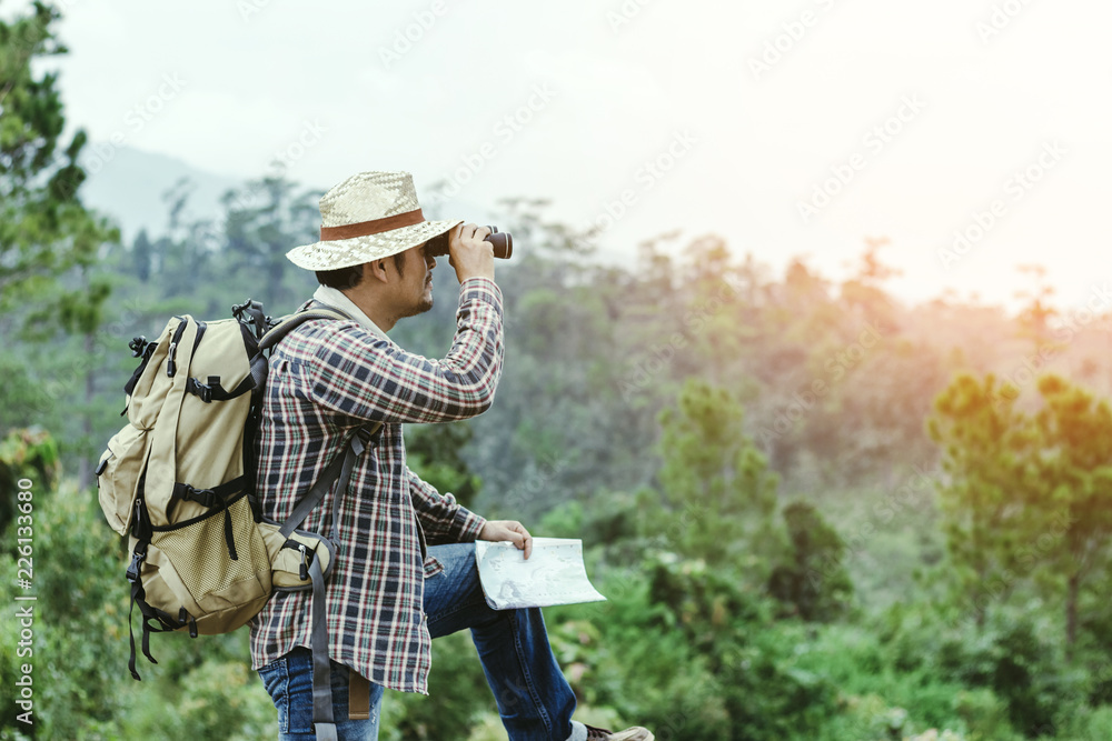 Young man with backpack and holding a binoculars standing on top of mountain