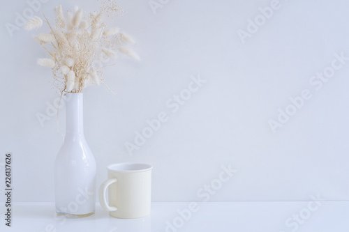 Mockup white glass vase with hay flower and yellow mug on white table