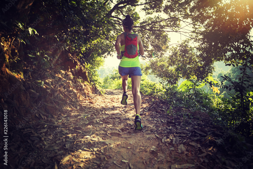 Obraz premium Young woman trail runner running on tropical forest trail during morning