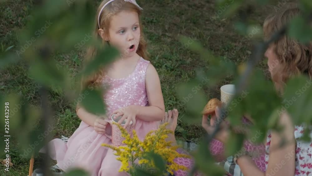 A happy mother and daughter are drinking tea on the veil. Family in a city park on a picnic on a warm evening at sunset.
