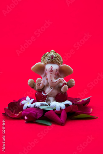 Lord Ganesha Idol with rose petals on red background, ganesh chautrhi, ganesh pooja