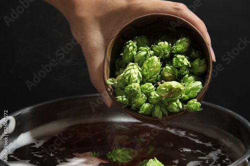 Fotografia Woman adding fresh green hops to beer wort in pot, closeup