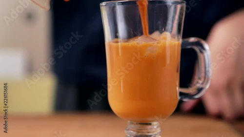 Pitcher pours Thai iced tea into a glass