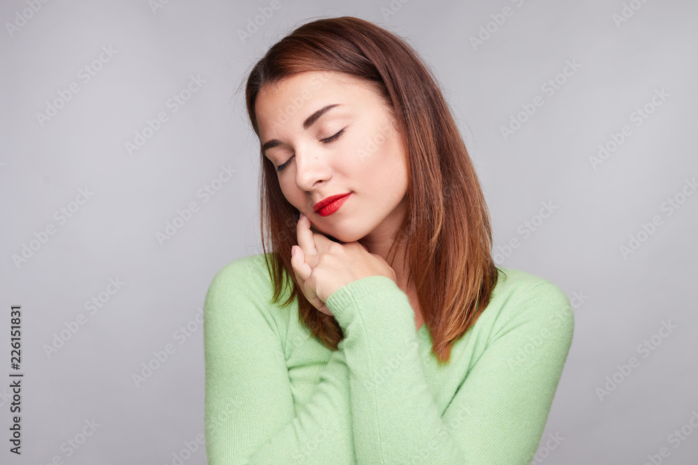 People, unexpectedness and emotions concept. Pleased European woman clasps hands from happiness, has tender smile full of delight, closing eyes in enjoyment, dressed in green cashmere sweater indoors People, unexpectedness and emotions concept. Pleased European woman clasps hands from happiness, has tender smile full of delight, closing eyes in enjoyment, dressed in green cashmere sweater indoors