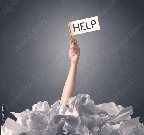 Female hand emerging from crumpled paper pile holding help sign 