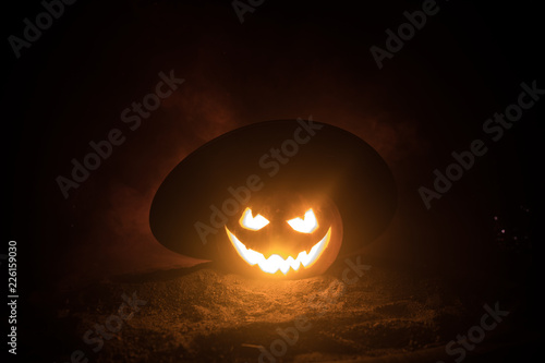 Halloween concept. Jack-o-lantern smile and scary eyes for party night. Close up view of scary pumpkin with witch hat on at dark foggy background. Selective focus. © zef art