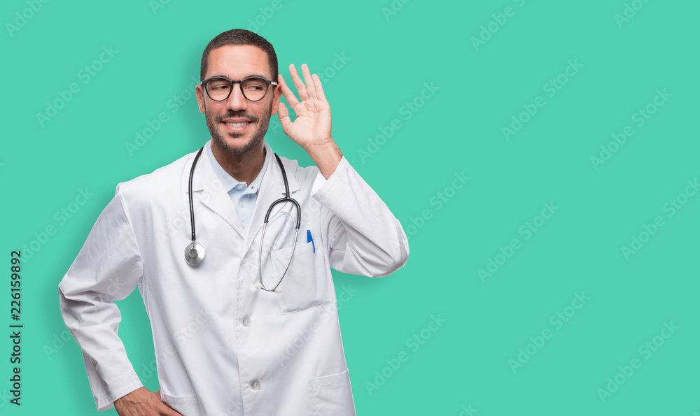 Happy young doctor with a gesture of trying to listen with his hand Happy young doctor with a gesture of trying to listen with his hand