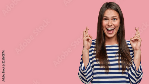 Fotografia Studio shot of cheerful brunette girl has overjoyed facial expression, keeps fin