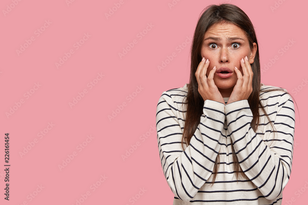 Studio shot of emotional frightened girl worries, has bated breath, keeps hands near mouth, isolated over pink background with free space aside for your advertisement or promotional content. Studio shot of emotional frightened girl worries, has bated breath, keeps hands near mouth, isolated over pink background with free space aside for your advertisement or promotional content.
