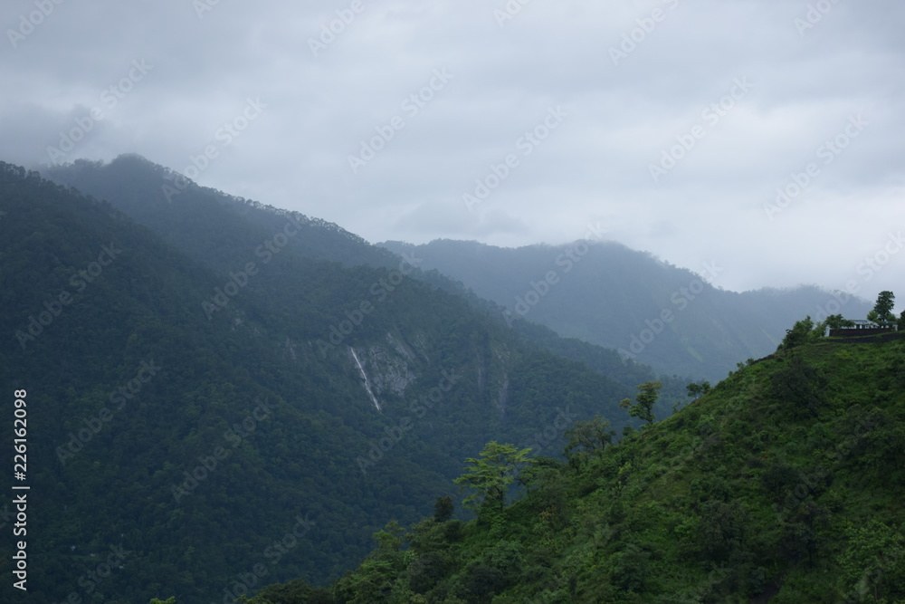 mountain ranges with trees in forground clouds and blue sky