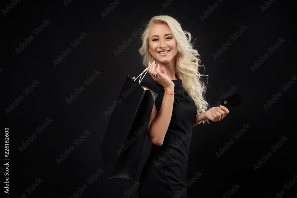 Elegant blonde woman wears black dress holding black shopping bags and credit card, black friday concept Elegant blonde woman wears black dress holding black shopping bags and credit card, black friday concept