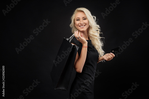Elegant blonde woman wears  black dress holding black shopping bags and credit card,  black friday concept