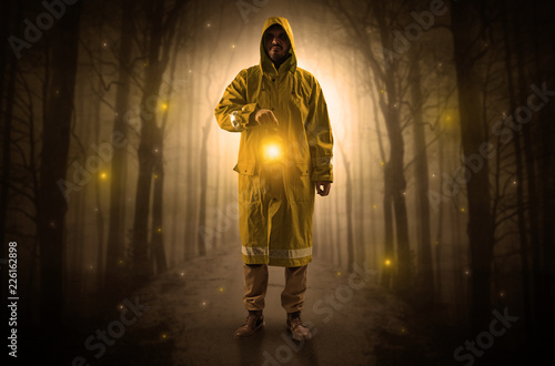 Man in raincoat coming from dark forest with glowing lantern in his hand concept 