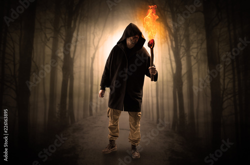 Mysterious man coming from a path in the forest with burning flambeau concept 