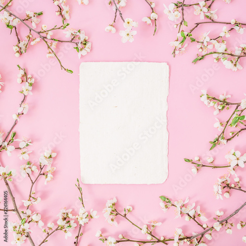 Floral frame with spring flowers and paper card on pastel pink background. Flat lay, top view. Spring background.