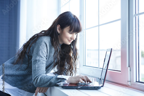 Middle-aged pretty woman is working with the PC notebook at home near the window