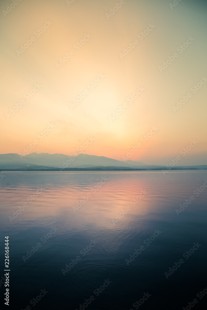 A beautiful, calm morning landscape of lake and mountains in the distance. Colorful summer scenery with mountain lake in dawn. Tatra mountains in Slovakia, Europe.