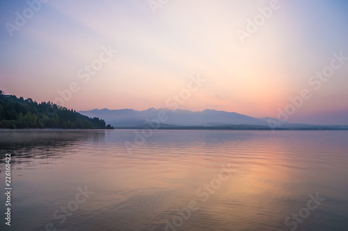 A beautiful, calm morning landscape of lake and mountains in the distance. Colorful summer scenery with mountain lake in dawn. Tatra mountains in Slovakia, Europe.