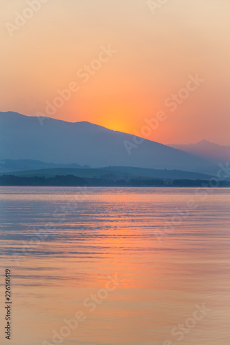 A beautiful, calm morning landscape of lake and mountains in the distance. Colorful summer scenery with mountain lake in dawn. Tatra mountains in Slovakia, Europe.