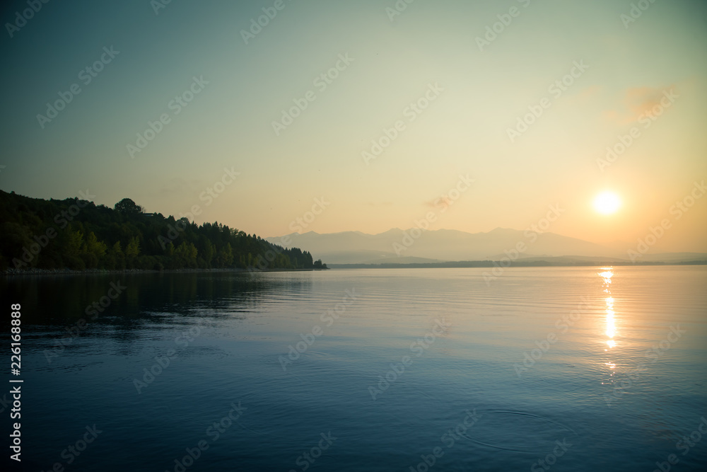 A beautiful, calm morning landscape of lake and mountains in the distance. Colorful summer scenery with mountain lake in dawn. Tatra mountains in Slovakia, Europe.