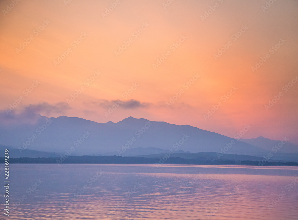 A beautiful sunrise over the lake with mountains in distance. Morning landscape in warm tones. Tatra mountains in Slovakia, Europe. A beautiful sunrise over the lake with mountains in distance. Morning landscape in warm tones. Tatra mountains in Slovakia, Europe.