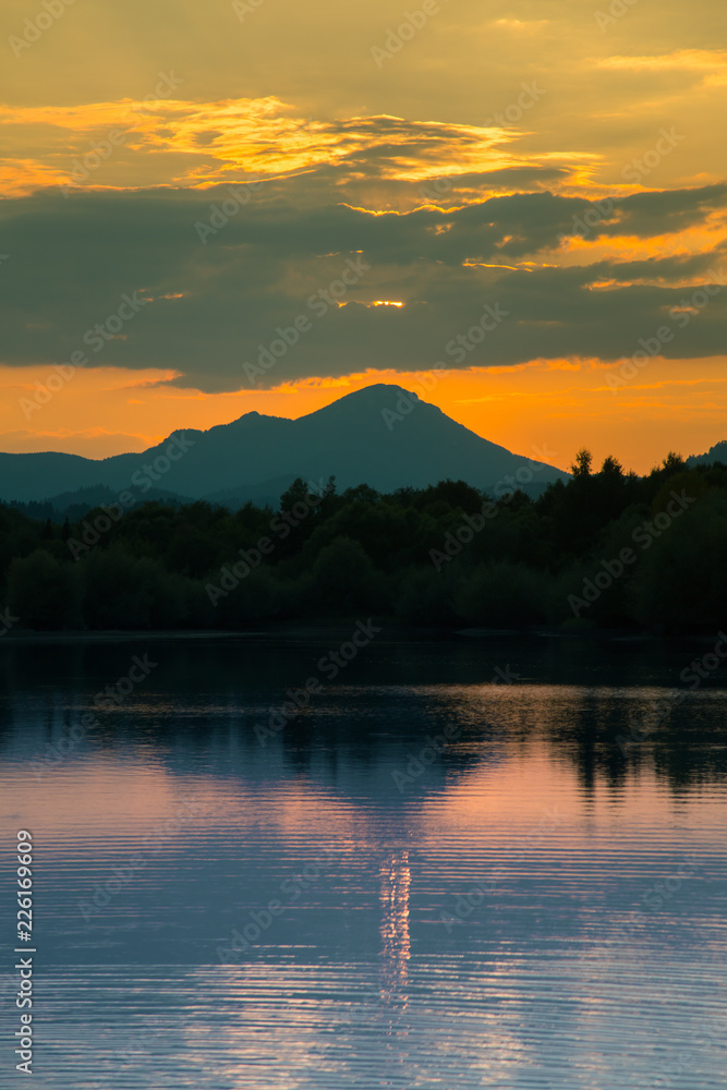 Obraz premium A beautiful, colorful sunset landscape with lake, mountain and forest. Natural evening scenery over the mountain lake in summer. Tatra mountains in Slovakia, Europe.