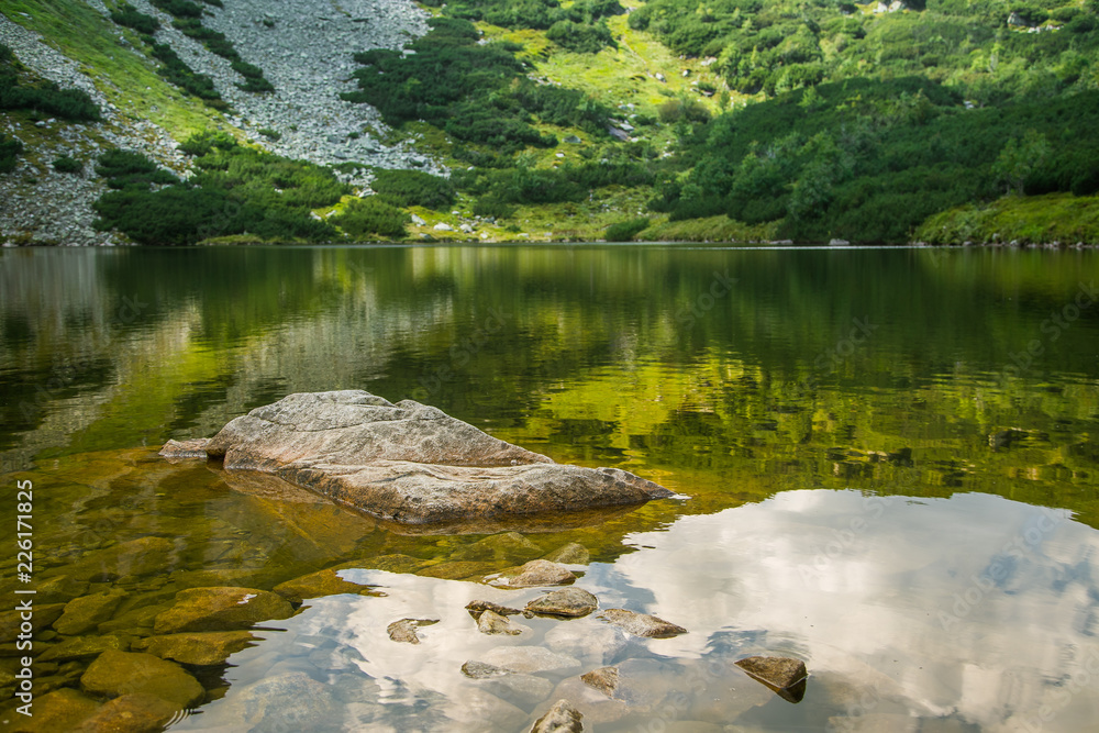 A beautiful, clean lake in the mountain valley in calm, sunny day. Mountain landscape with water in summer. Tatry mountains in Slovakia, Europe. A beautiful, clean lake in the mountain valley in calm, sunny day. Mountain landscape with water in summer. Tatry mountains in Slovakia, Europe.