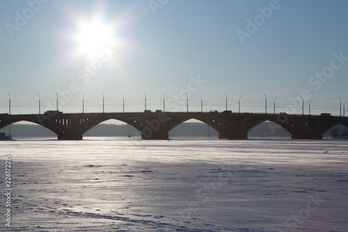 Concrete bridge over the river. The river is frozen. The cars are driving along the bridge.