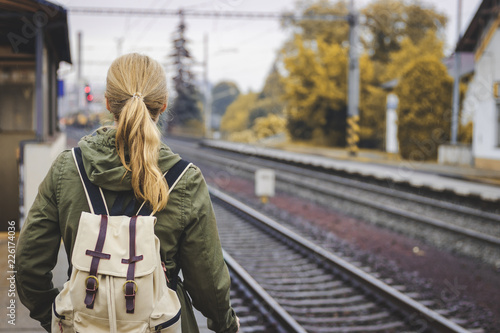 Woman with backpack standing at railroad station platform and waiting for a train. Travel concept 