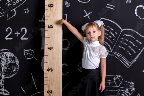 Coquette schoolgirl standing before the chalkboard as a background pointing to the huge scale photo