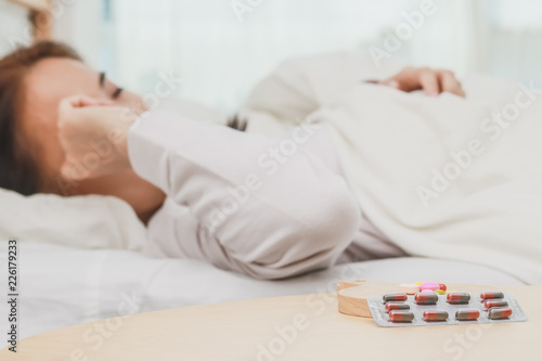 Closeup on pills and glass of water on table and Asian women sleep sick on bed in bed room