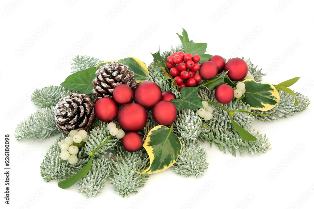 Christmas table decoration with red bauble decorations, holly berries, snow covered spruce pine, ivy, pine cones and mistletoe isolated on white background.