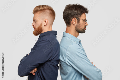 Indoor view of serious two partners stand back, have some disagreement, keeps hands folded, cant find common solution, have common business, isolated over white background. Partnership concept