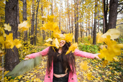 Autumn, joy and people concept - young woman having fun in autumn park. She is throwing yellow leaves in a sky