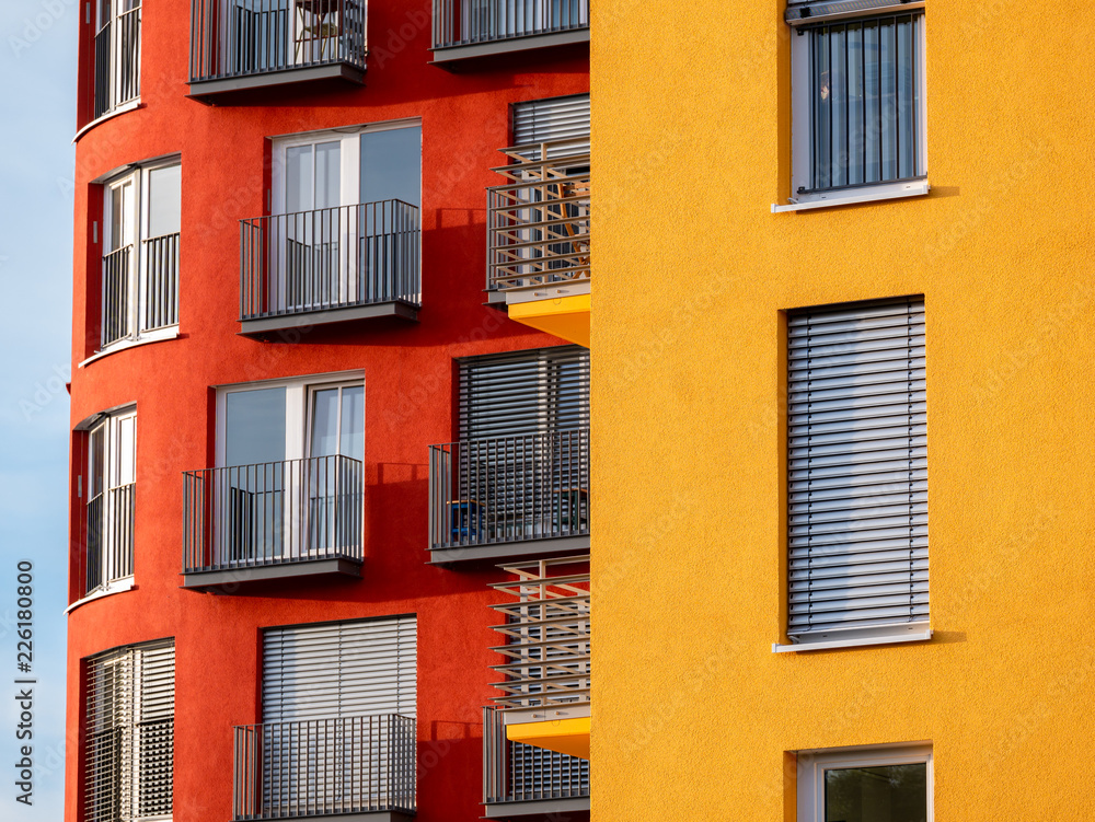 Image of two red and yellow high rise buildings with windows and balconies and blinds