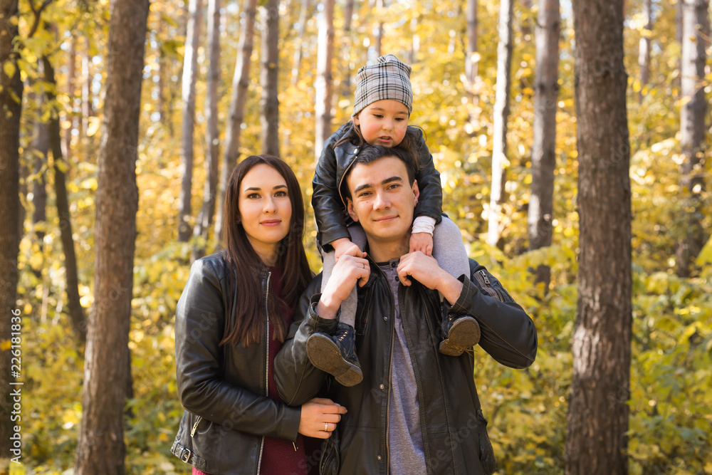 Family, autumn, people concept - young family walking in autumn park. Daughter sitting on dad's shoulders Family, autumn, people concept - young family walking in autumn park. Daughter sitting on dad's shoulders