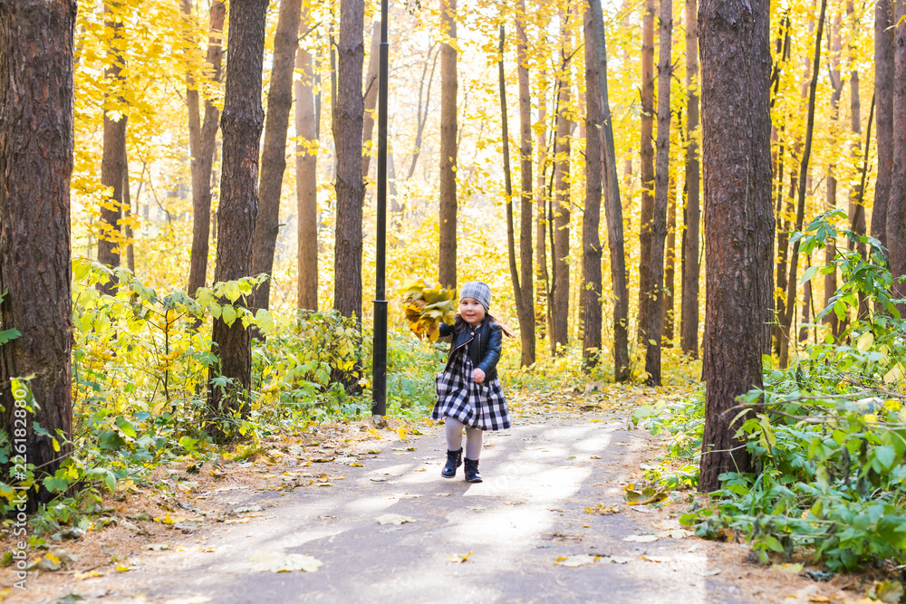 Autumn, happiness and people concept - child running through autumn park with yellow leaves in her hands