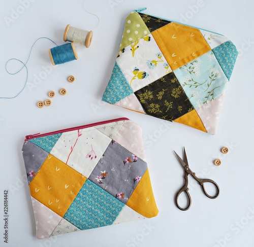 Patchwork notions bags, wooden buttons, retro scissors and vintage thread spools on white