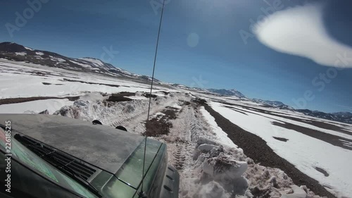 4x4 van going through snowy gravel road at winter on The Andes altiplane. Wide Valley, mountains and volcanoes with snow at background. Adventure excursion to Brava Lagoon. Rioja Province photo