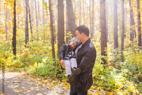 Fatherhood, family and leisure concept - father holding little daughter in his arms in autumn park